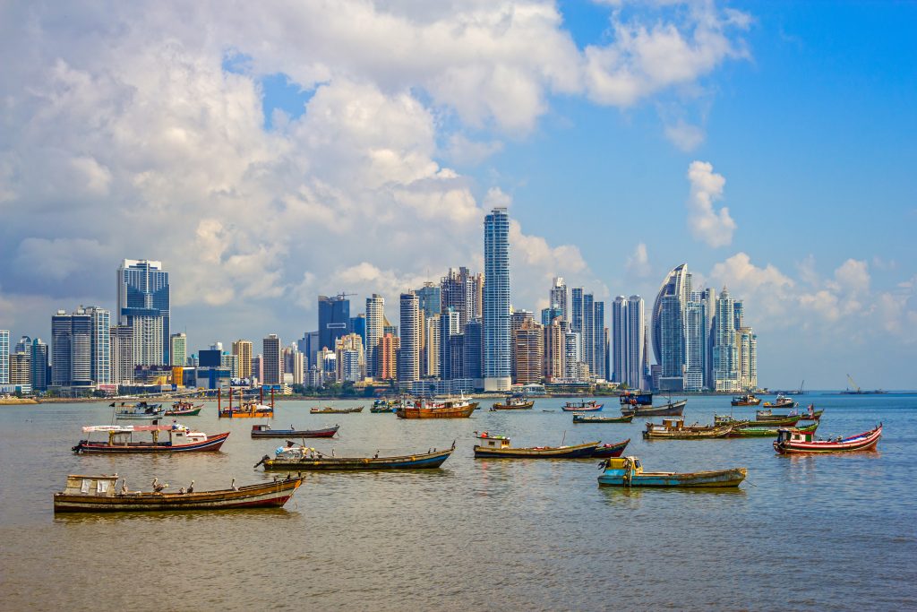 A group of nearly two dozen fishing boats anchored in the bay with Panama City's skyline in the background.